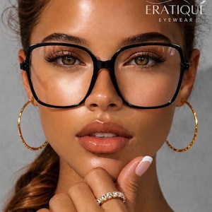May include: Oversized black square-framed glasses with clear lenses featuring the text ERATIQUE EYEWEAR in the upper right corner. The glasses are paired with large gold hoop earrings and a gold band ring set with small clear stones.