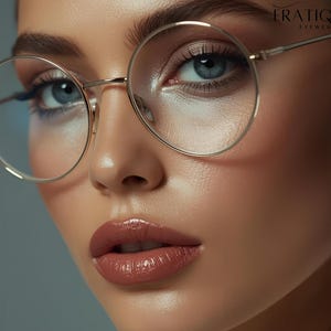 May include: Close-up of a person wearing round, gold-rimmed eyeglasses. The glasses have clear lenses and are set against a soft, neutral background. The image also features the brand name "ERATIQUE EYEWEAR" in the upper right corner.