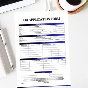 May include: A printed job application form with a blue and black header and sections for personal information, employment desired, education, previous employment, and skills. A pen and a notepad are on the white surface.