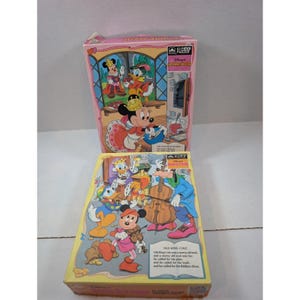 May include: Two Disney 63-piece jigsaw puzzle boxes. The top box features Minnie Mouse as the Queen of Hearts in a kitchen. The bottom box depicts Uncle Scrooge, Donald Duck, and Goofy playing musical instruments with the text Old King Cole.