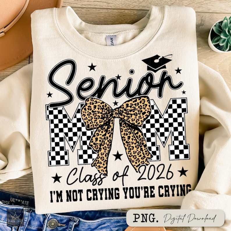 May include: Cream-colored sweatshirt with the text "Senior Mom" in black script and block letters, featuring a leopard print bow. Includes "Class of 2026" and the phrase "I'M NOT CRYING YOU'RE CRYING".