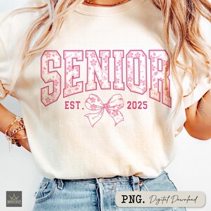 Pu&ograve; includere: Felpa color crema con la scritta "SENIOR" in rosa, con lettere a motivi floreali. Sotto c'&egrave; "EST. 2025" e una grafica a fiocco rosa. L'immagine ha un'etichetta di download digitale PNG.