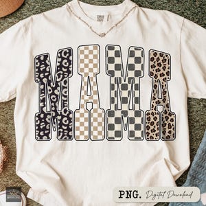 May include: Cream-coloured t-shirt with the word "MAMA" in a bold, block letter design. The letters feature various patterns, including leopard print and checkered designs. The shirt has a crew neck and short sleeves.