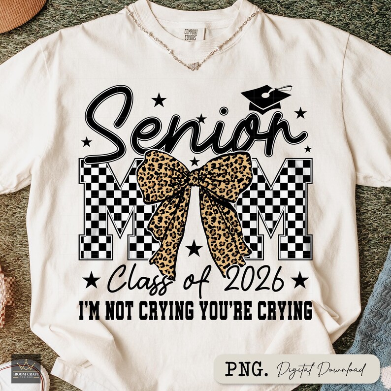 May include: Cream-colored t-shirt with a black and leopard print design. The design includes the word "Senior", the letters "MOM", a graduation cap, stars, and the text "Class of 2026" and "I'M NOT CRYING YOU'RE CRYING".