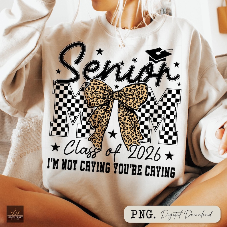 May include: Cream-colored sweatshirt with the text "Senior Mom" in black script, a graduation cap, and the words "Class of 2026." A leopard print bow is centered on the design, with the phrase "I'm not crying you're crying" below.