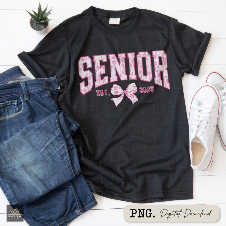 Pu&ograve; includere: T-shirt nero con la scritta "SENIOR" in lettere floreali rosa, "EST. 2025" sotto e un fiocco rosa. La maglietta &egrave; abbinata a jeans blu e scarpe da ginnastica bianche. &Egrave; visibile anche una piccola pianta in vaso.