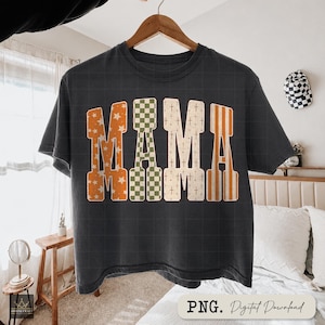 Może przedstawiać: Ciemnoszary t-shirt z krótkim rękawem z napisem MAMA wydrukowanym dużymi literami blokowymi. Każda litera ma inny wzór: pomarańczowy w białe gwiazdki, zielono-białą szachownicę, beżowy w małe krzyżyki oraz pomarańczowe paski.