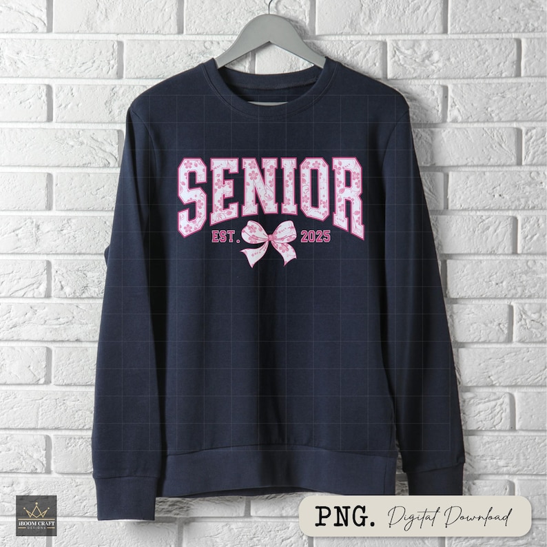 Pu&ograve; includere: Felpa blu navy con la scritta "SENIOR" in lettere floreali rosa. Sono presenti anche il testo "EST. 2025" e un fiocco rosa. La felpa &egrave; appesa a una gruccia grigia contro un muro di mattoni bianchi.
