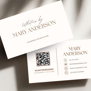 May include: Two business cards with a cream background and brown text. The top card reads "Esthetics by MARY ANDERSON, LICENSED ESTHETICIAN." The bottom card includes contact information, a QR code, and the text "SCAN FOR BOOKING 123 ANYWHERE ST, CITY ST 12345."