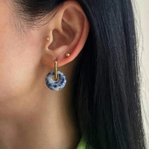 May include: Gold hoop earrings with a blue and white stone pendant. The stone has a speckled pattern.