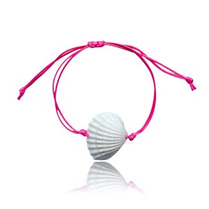 May include: A bracelet featuring a single white ridged seashell centred on a vibrant hot pink cord. The cord is adjustable with sliding knots on each side, allowing for a flexible fit. The shell has a natural texture with subtle tan markings.