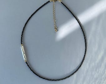 May include: A delicate necklace featuring a strand of small, faceted black beads accented by a single elongated white pearl bead. The piece includes a gold-toned metal lobster clasp and an adjustable chain extender for a customisable fit.