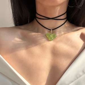 May include: A black choker necklace with a green butterfly pendant. The necklace is layered and features a delicate gold chain.