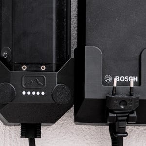 Könnte beinhalten: Zwei schwarze Akkus mit eingesteckten Ladekabeln. Der Akku links hat ein kleines Berglogo und eine Reihe von fünf weißen Lichtern. Der Akku rechts hat den Schriftzug "BOSCH" aufgedruckt.
