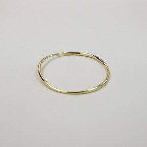 May include: A gold-colored bangle bracelet with a slightly irregular, wavy design. The bracelet is a simple, circular band, likely made of metal, and is set against a plain, light background. The jewelry piece is a minimalist accessory.