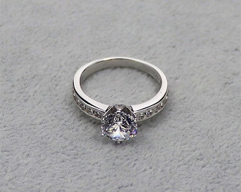May include: A silver ring with a single large clear stone surrounded by smaller clear stones.