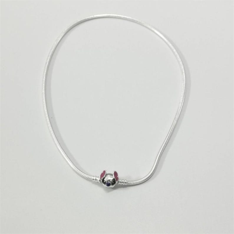 May include: A silver necklace featuring a charm of a cartoon character's face with pink ears and a blue face. The necklace is made of a thin, flexible silver chain.