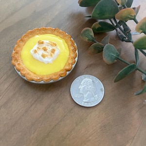 Puede incluir: Un mini pastel de limón merengue con un relleno amarillo y una cobertura de merengue blanco. El pastel está en una corteza de pastel acanalada y está sobre una superficie de madera.