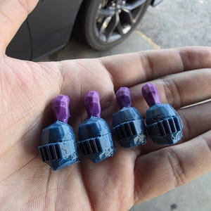Puede incluir: Cuatro pequeños cascos de caballero en miniatura impresos en 3D de color azul oscuro con penachos morados en la parte superior. Cada casco presenta un diseño de visera clásico con barras verticales y un acabado de superficie texturizado.