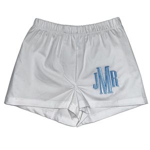 May include: White boxer shorts with an elastic waistband and a blue embroidered monogram. The shorts are made of a soft, lightweight fabric. The monogram features the letters JMR.