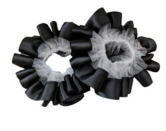 May include: Two black satin scrunchies with white lace trim. The scrunchies are circular and have multiple layers of folded satin. The white lace is visible in the center of each scrunchie.