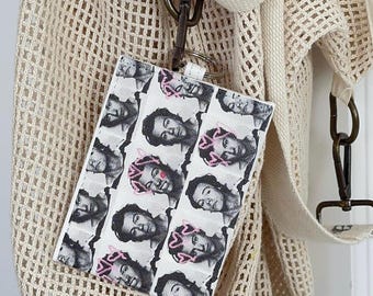 May include: A white canvas tote bag with a mesh design. A small white card holder with a repeating pattern of black and white faces is attached to the bag.
