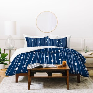 May include: A navy blue duvet cover with a white geometric pattern of lines and circles. The duvet cover is on a bed with white pillowcases and a wooden bed frame.
