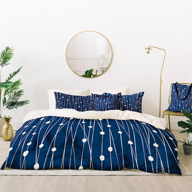 May include: A navy blue duvet cover with a white minimalist line and dot pattern.  The bedding set includes matching pillow shams. The duvet cover and shams feature a modern, geometric design. The overall aesthetic is clean and sophisticated, suitable for a contemporary bedroom.  Gold accents are visible in the room's decor, including a round mirror and floor lamp.