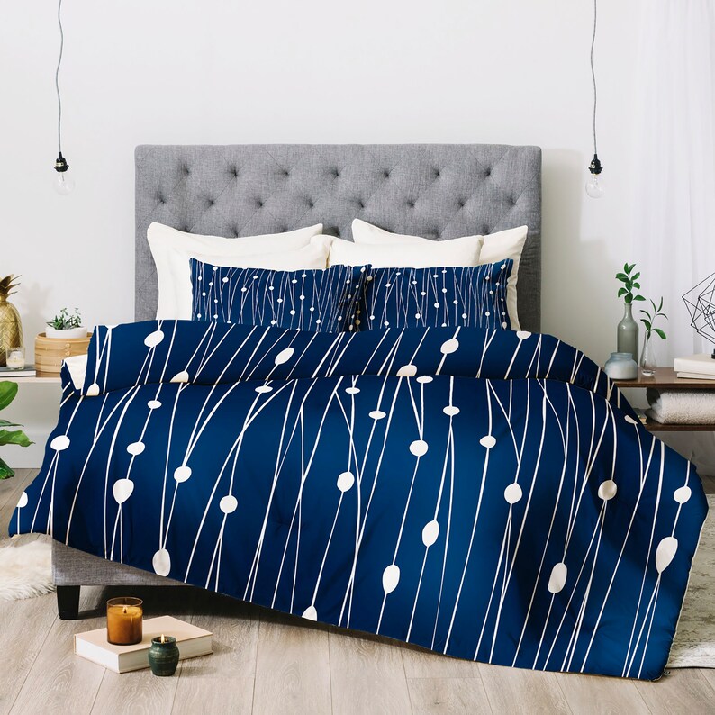 May include: A navy blue duvet cover with a white geometric pattern of lines and circles. The duvet cover is on a bed with white and cream pillows.