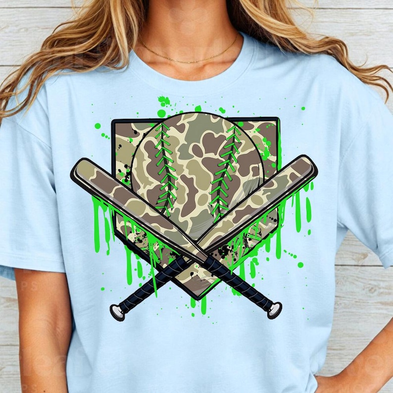 May include: Light blue t-shirt featuring a green and brown camouflage baseball and crossed bats graphic. The graphic has green paint splatters around it.