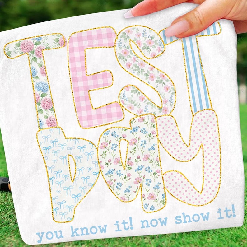 May include: White fabric with the words "TEST DAY" in large, colorful letters. The letters are decorated with floral, gingham, polka dot, and striped patterns, outlined in gold glitter. The text "you know it! now show it!" is printed below.