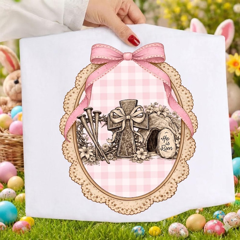 May include: White Easter-themed fabric featuring a pink gingham pattern and a cross design. The design includes a pink bow, nails, and the text "He is Risen" in an oval frame with a lace border. The fabric is held by a person.