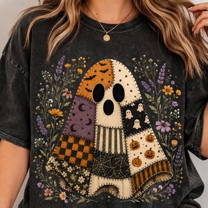 May include: A charcoal grey mineral-washed t-shirt featuring a large central graphic of a patchwork ghost. The ghost is composed of various patterns including orange bats, purple moons, black and orange checkers, spiderwebs, and pumpkins.