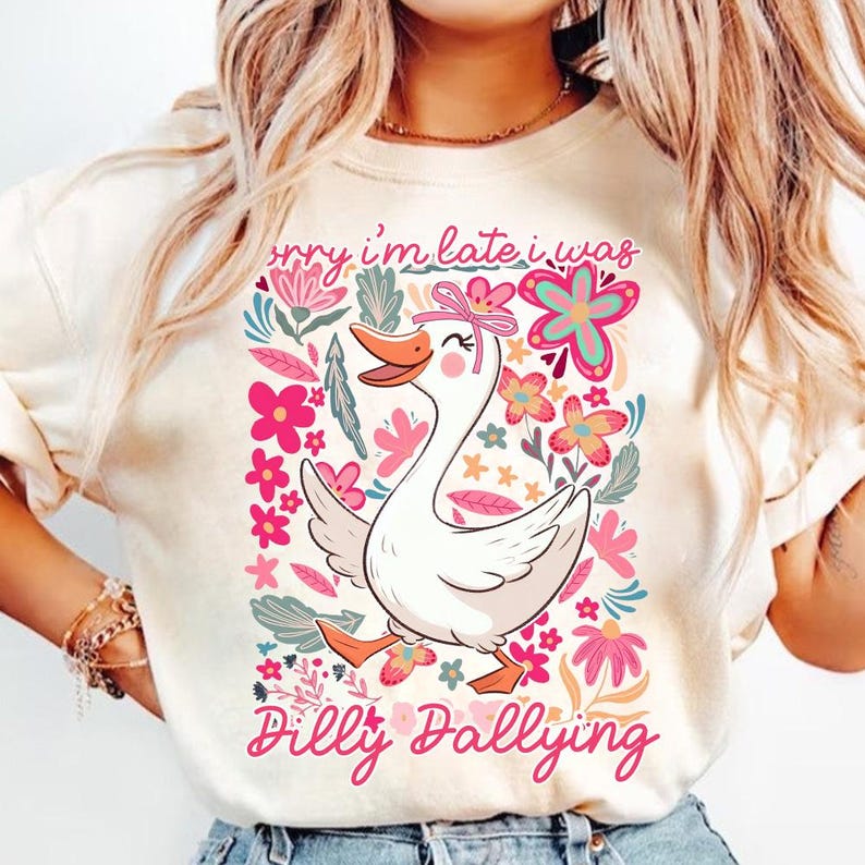 K&ouml;nnte beinhalten: Cremefarbenes Sweatshirt mit einer skurrilen Grafik einer wei&szlig;en Gans mit rosa Schleife, umgeben von bunten Blumen. Der Text "Sorry I'm late I was Dilly Dallying" steht in rosa Schrift darunter.