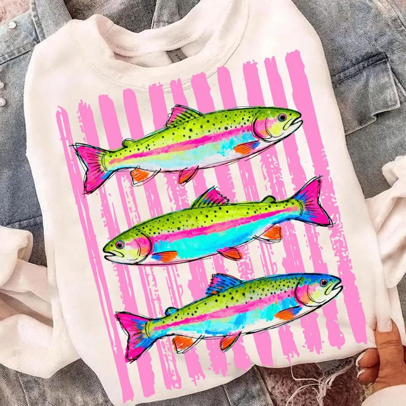 May include: White sweatshirt featuring a colorful graphic of three rainbow trout. The fish have green, blue, pink, and orange details, set against a background of pink vertical stripes. A casual and vibrant design.