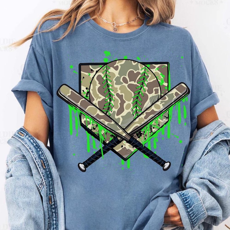 May include: A blue t-shirt featuring a green camouflage baseball and crossed bats graphic. The graphic has green paint splatters and drips.