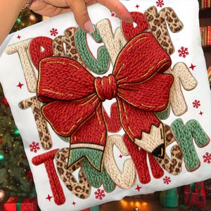 May include: White decorative pillow with the word "TEACHER" in various styles. A large red bow and pencil are in the center. The letters are in red, green, tan, and leopard print. Red stars and snowflakes are scattered around the text.