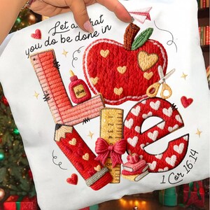 Puede incluir: Tela blanca con un diseño bordado con la palabra "LOVE" compuesta por elementos escolares. El diseño incluye una manzana roja, un lápiz, una regla, tijeras y corazones. También está presente el texto "Let all that you do be done in" y "1 Cor 16:14".