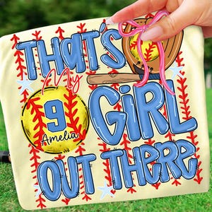 Op de afbeelding: Een lichtgeel honkbal-thema handdoek met de tekst "THAT'S MY GIRL OUT THERE" in blauwe bubbelletters. Een honkbalhandschoen en een knuppel zijn ook afgebeeld. Een honkbal met het nummer 9 en de naam "Amelia" staat in het midden.