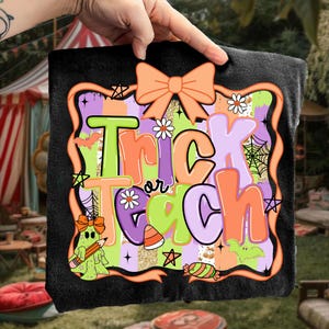 May include: Black Halloween-themed blanket with the words "Trick or Teach" in orange, green, and purple. The design includes a bow, stars, daisies, a ghost holding a pencil, and candy corn.