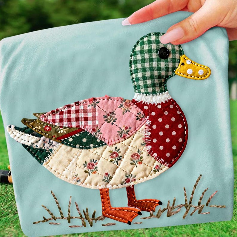 May include: A decorative duck applique with a patchwork design. The duck features a green and white checkered head, a red polka-dotted body, and a yellow beak. The wings are made of various patterned fabrics, and the duck is set against a light blue background.