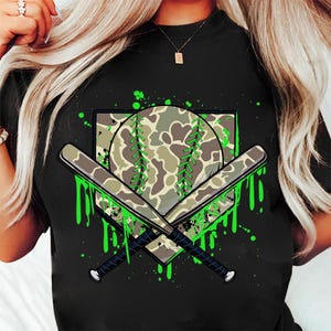 May include: Black t-shirt featuring a green camouflage baseball, two crossed bats, and green paint splatters.