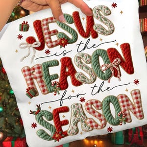 May include: A white cushion featuring the phrase "JESUS is the REASON for the SEASON." The letters are in festive red, green, and white, with Christmas decorations. The cushion is held by a person.