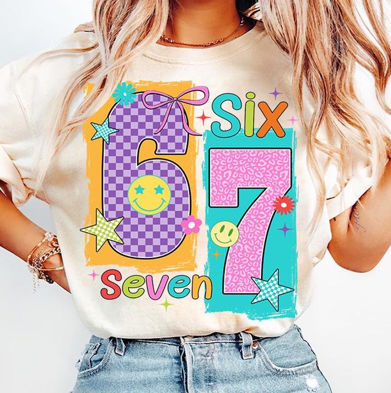 May include: Cream-coloured t-shirt with a colourful graphic design featuring the numbers "6" and "7". The number "6" is purple checkered, and the number "7" is pink leopard print. The word "Six" is in green and orange, and "Seven" is in red.
