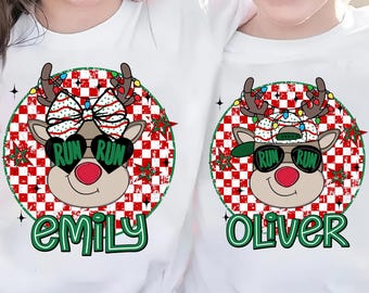 May include: White t-shirts featuring a Christmas reindeer design. The reindeer wears sunglasses with "Run Run", a red nose, and antlers adorned with lights. One shirt says "Emily" and the other says "Oliver" in green.