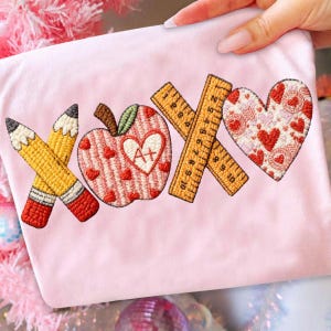 May include: Pink fabric with embroidered school-themed designs. Features a pencil, apple, crossed rulers, and a heart. The apple has a heart-shaped center with "A+" inside. The heart is decorated with hearts.