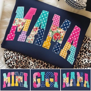May include: Navy blue sweatshirt with the word "MAMA" appliqued in colorful patchwork fabric. The letters feature floral, polka dot, and gingham patterns. Additional designs include "MIMI", "GIGI", and "NANA" in similar styles.