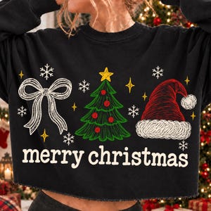 May include: A black long-sleeve sweatshirt featuring a white line-art bow, a green Christmas tree with red ornaments, and a red Santa hat. The text "merry christmas" is printed in white below the graphics, surrounded by small white snowflakes.
