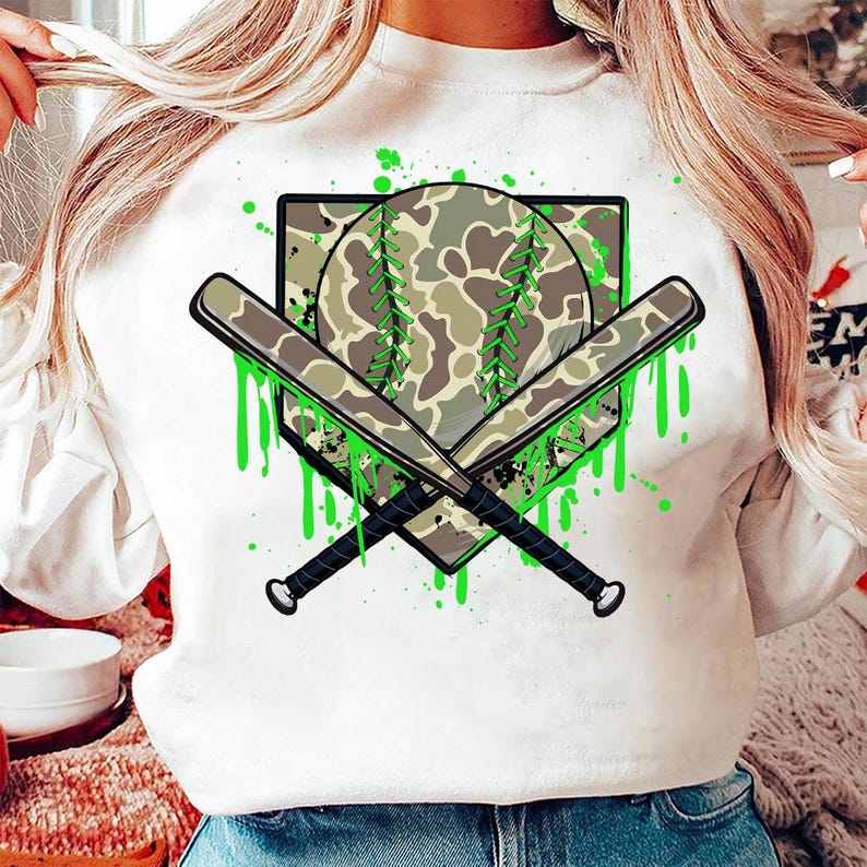May include: White sweatshirt featuring a green and camouflage baseball graphic. The graphic depicts a baseball with a camo pattern, two crossed bats, and green paint splatters.