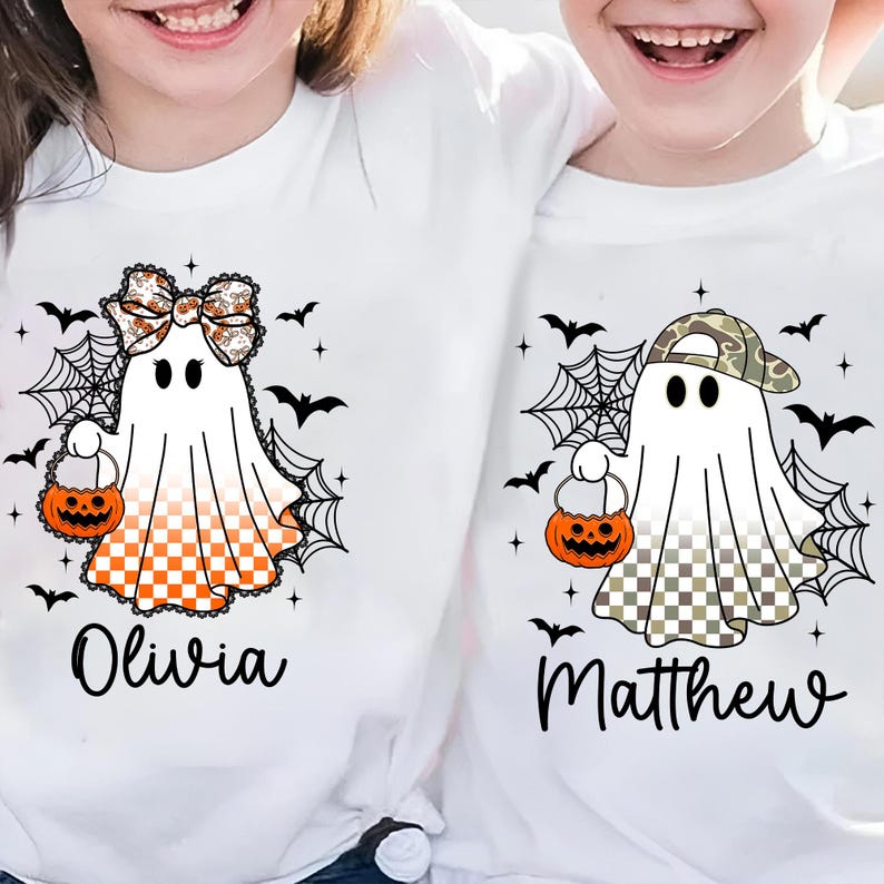 Puede incluir: Camisetas blancas con dise&ntilde;os de fantasmas de Halloween. Un fantasma tiene un lazo y una parte inferior a cuadros naranja y blanco, el otro lleva una gorra de camuflaje y tiene una parte inferior a cuadros. Ambos sostienen bolsas de golosinas de calabaza. Nombres "Olivia" y "Matthew".